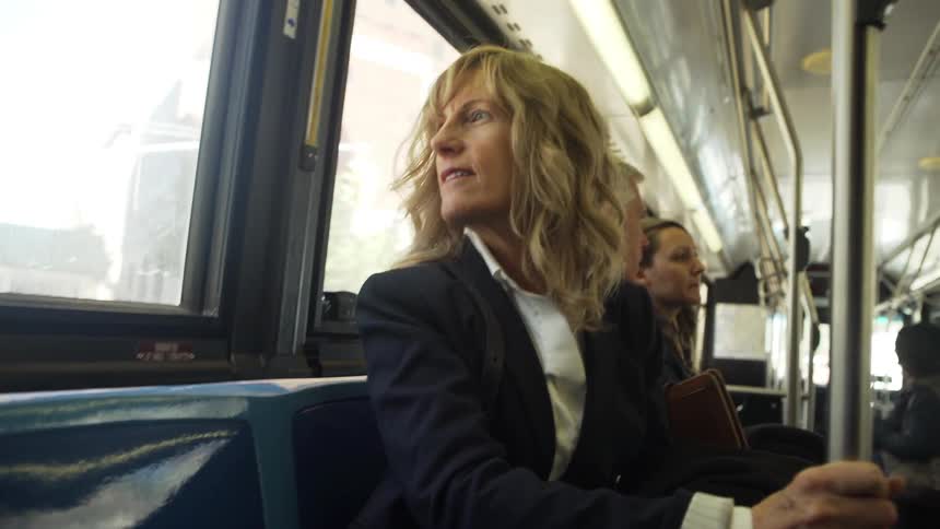 Woman holds a pole as she travels in a train as other passengers sit nearby
