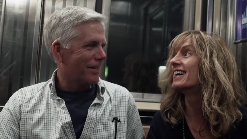 A man and a woman sit on a subway car and chat and smile