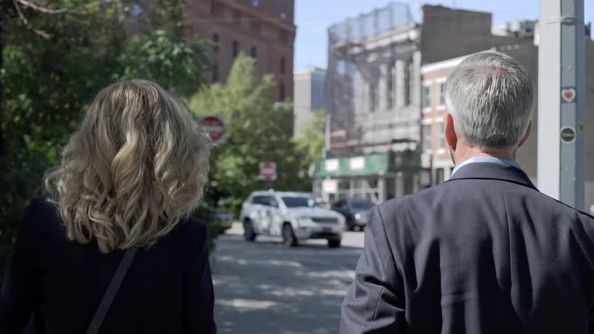 Man and woman in suits walk alongside city street