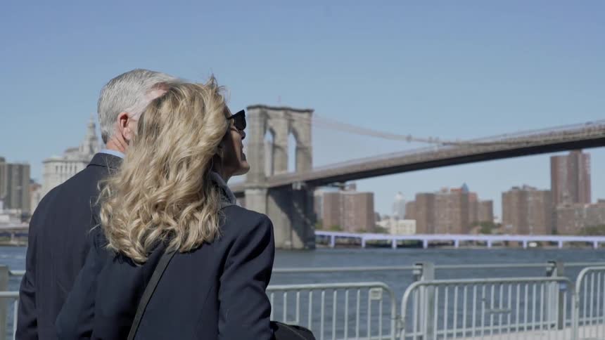 Older couple walks along river near brooklyn bridge