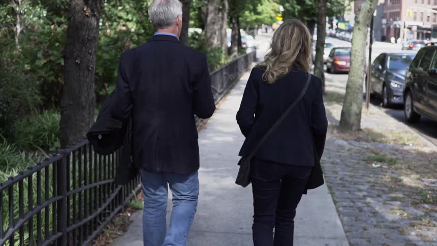 Couple walks down sidewalk near a park at day in city downtown