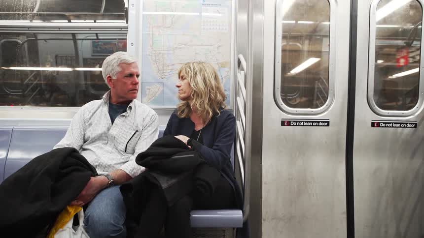 A man and woman sit on a subway and talk
