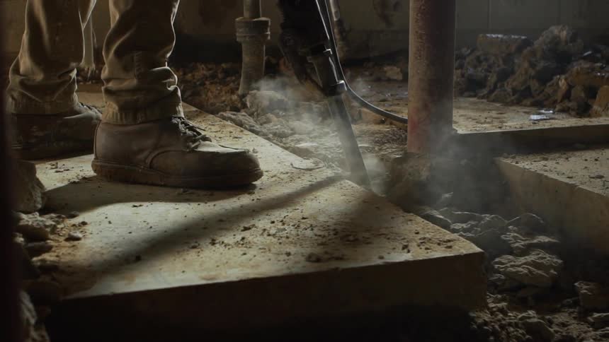 A worker uses a jackhammer to dig through concrete in a basement