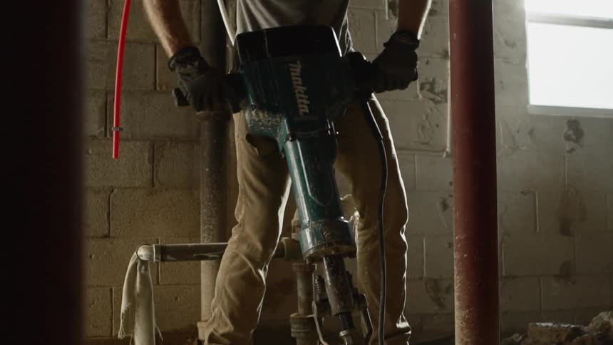 Construction worker using jackhammer to break up concrete in building