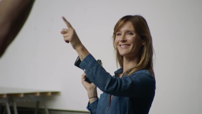A white woman with a camera points her finger and speaks with a white male
