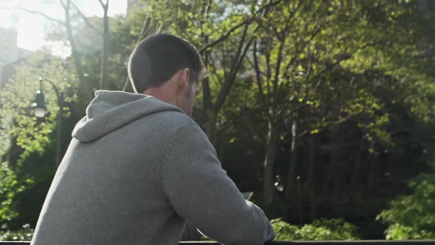 Man looking at cell phone leaning on railing in public park