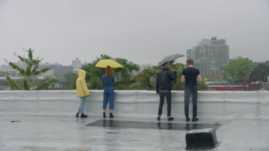 Four friends walk around on the roof of a building in a city when it is raining