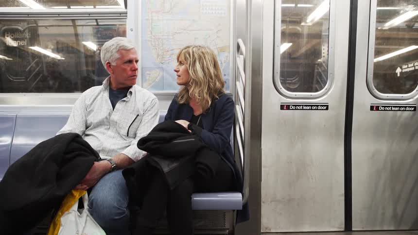 Male and female couple sit closely together on the seat of the subway and have a conversation together as the door begins to close and the train starts to move