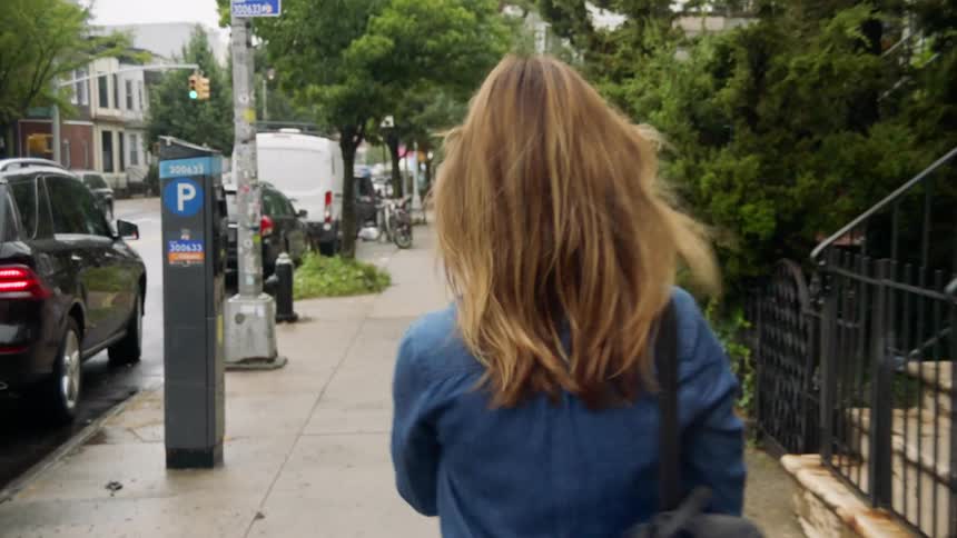 A woman walks down a sidewalk with her purse in the city