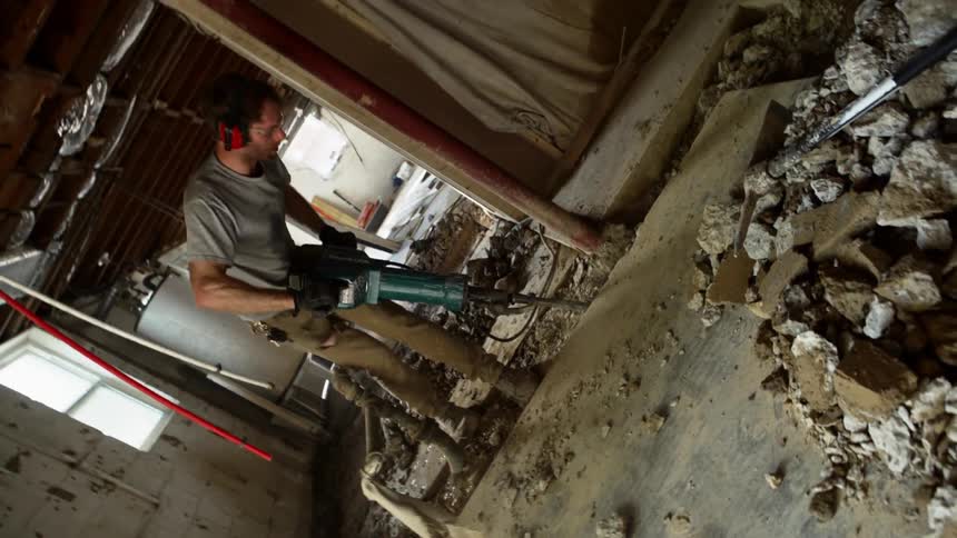 Worker uses a jackhammer to break the concrete on the floor of a building