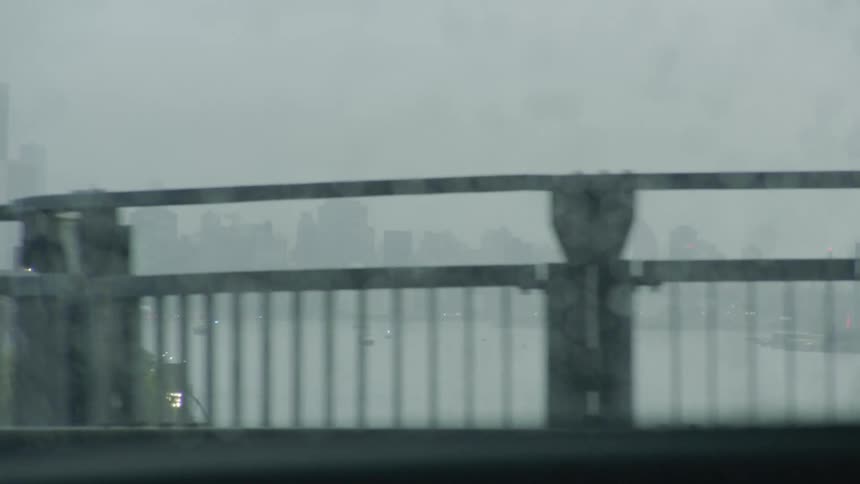 A river and a city skyline are visible from a car traveling across a bridge