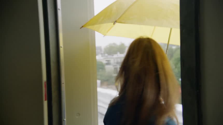 A woman opens up an umbrella as she and a man leave their apartment and walk outdoors in the rain