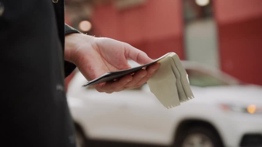 A man on a city street holds papers and takes out his cell phone