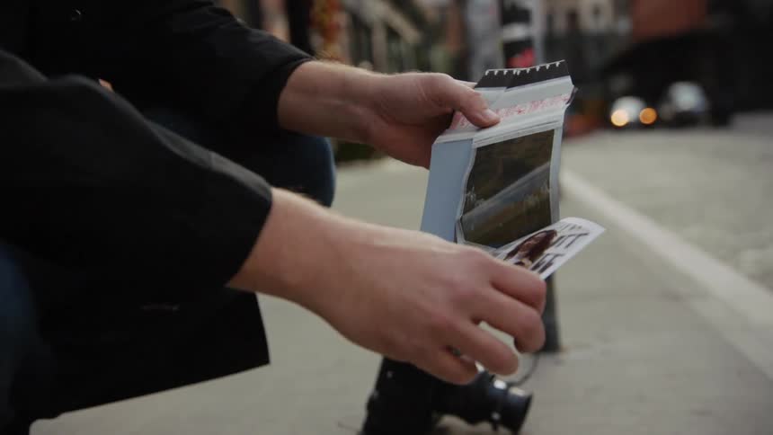A photographer rips the film about from a photo kneeling on a sidewalk