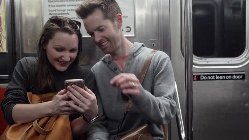 Young couple on subway looking at cell phone and smiling