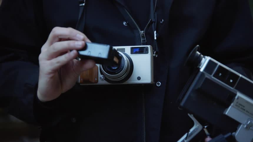 A white person takes a film roll out of a film camera and then turns to walk off