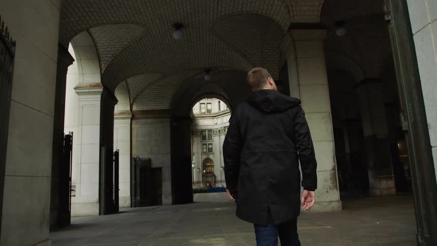 Man holding digital camera walks through large arched breezeway of building