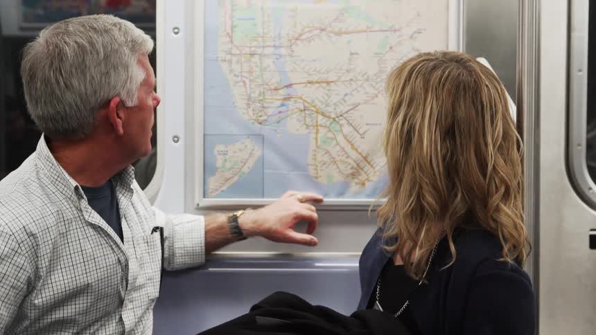 A man points to a map on a subway to a woman sitting next to him