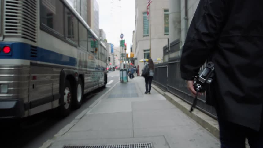 A man walks down a city street holding a camera