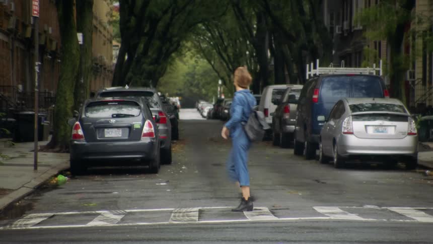 A woman crossing a city street with vehicles and buildings in the background