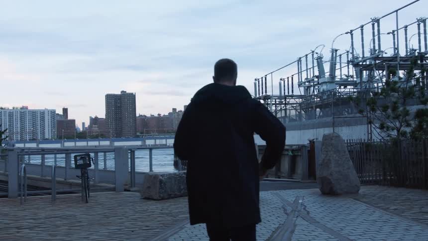 Man walks on path near river and electrical substation at dusk