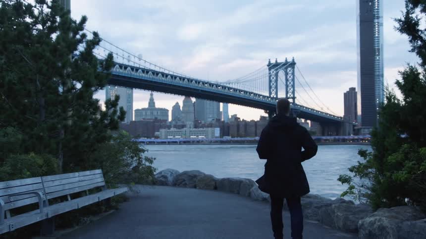 Man walks along river in front of manhattan bridge at dawn