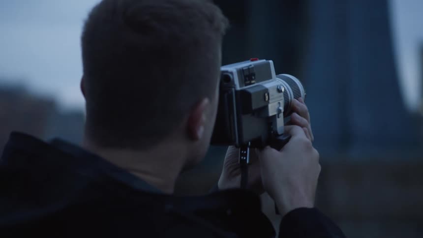 A man holds a camera up to his face and looks toward a large city