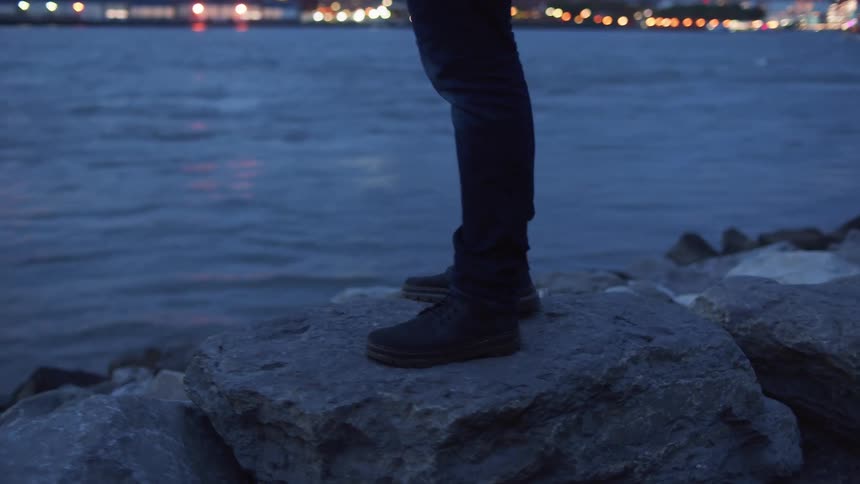Man stands on a rock and watches the skyline across the sea