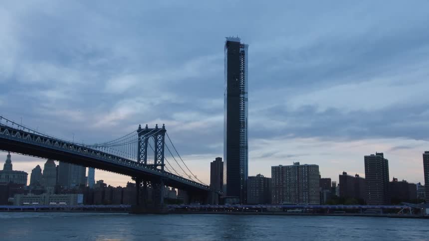 A skyscraper stands at the end of a city bridge over water