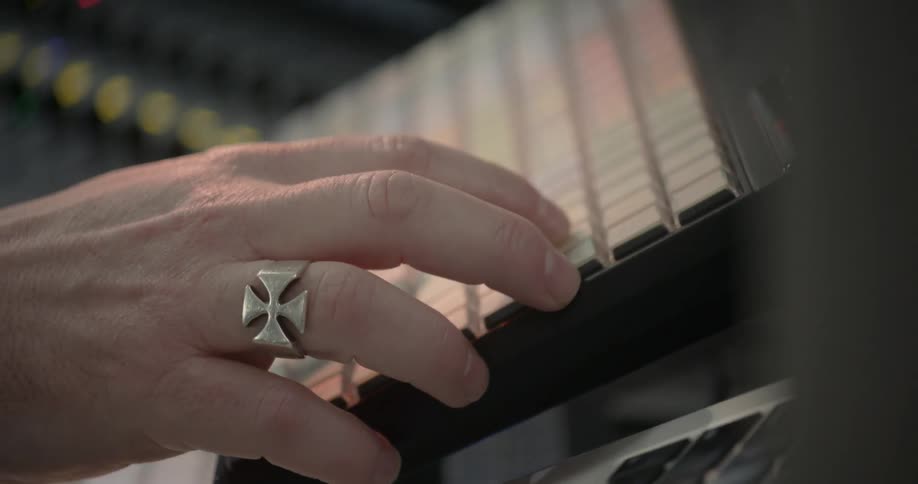 A white man punches buttons on a keyboard in a sound studio