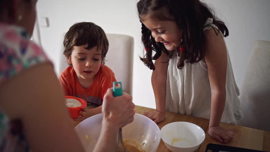 Two small children help an adult mix food in a bowl