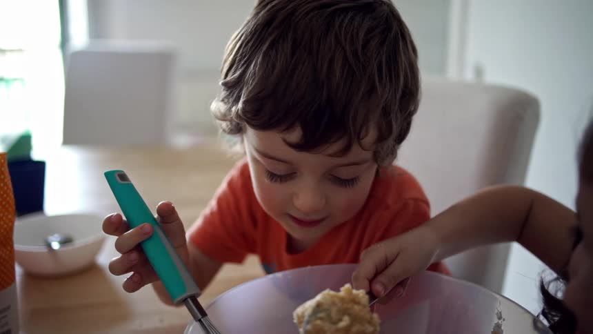A boy and a girl mixing food in a mixing bowl