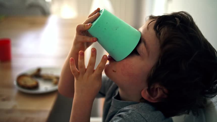 A young boy is drinking from a green cup