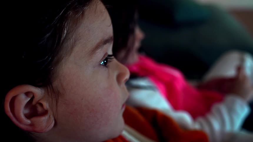Two little girls sitting in a couch watch television at home