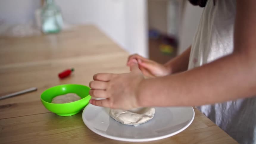 Girl plays with modeling clay on a plate over a table at home