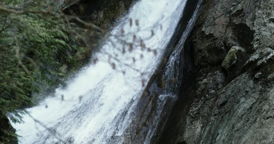 Waterfall flows down stone slightly sloping cliff face