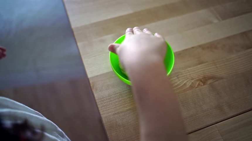 A young white girl rubs a wad of dough in a green bowl