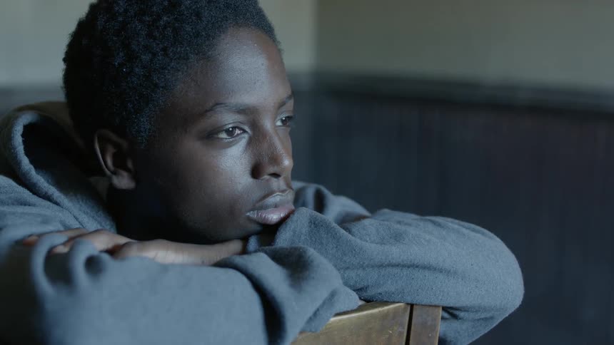 A young man sitting backwards in a chair gazing at a window while lost in thought