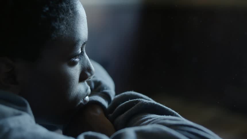 A man sits in a dark room with his arms crossed and his chin resting on his hands