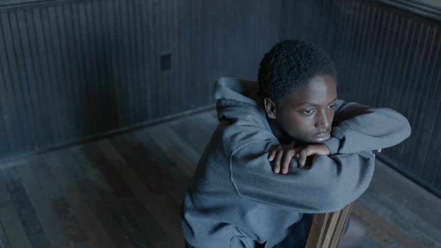 A boy sitting backwards on a chair resting his chin on his crossed arms while lost in thought