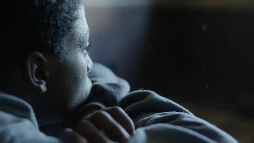 Youth wearing hoodie rests head on crossed arms