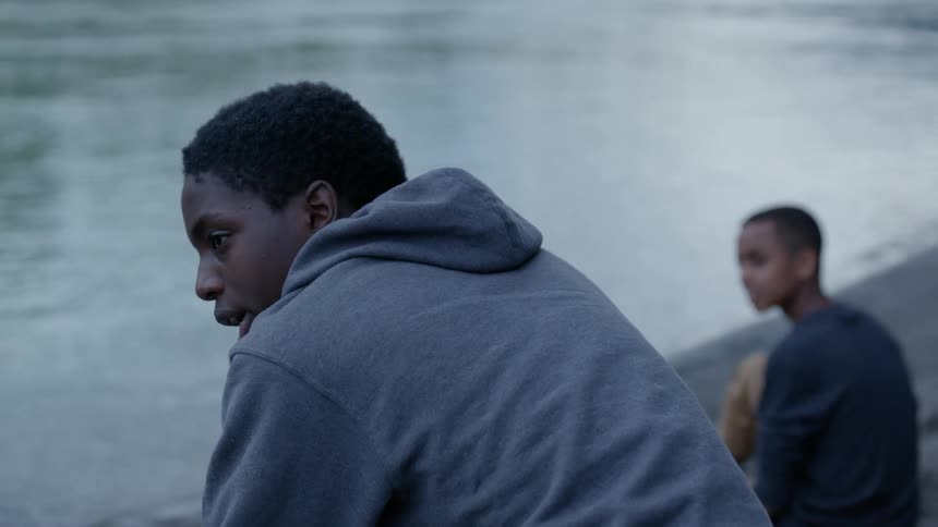 Two boys sit in front of a lake talking