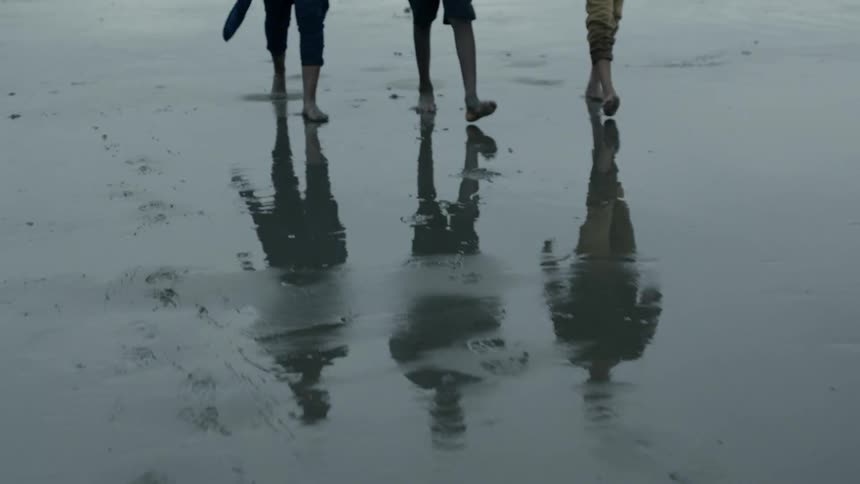 Friends walk across the wet sand beach on a rainy day