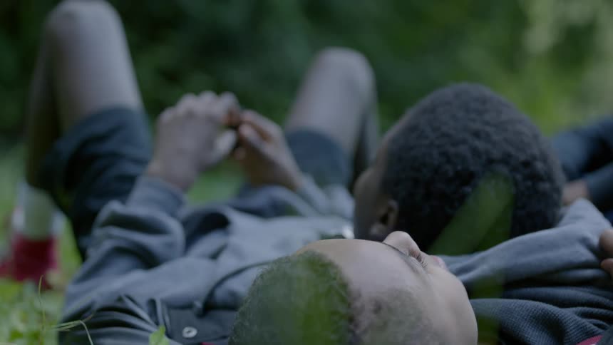 A young man lying in the grass talking with his younger brother who is resting their head on his chest