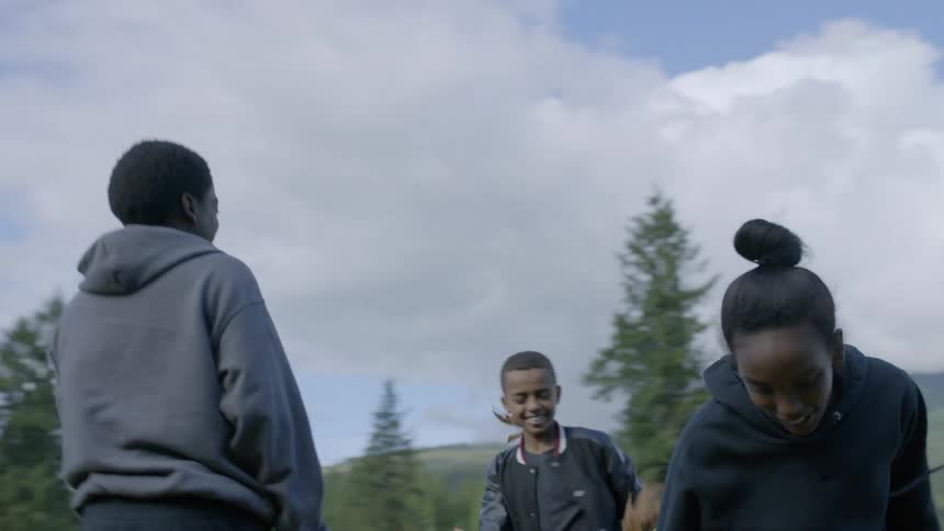 Three children throw leaves at each other in a large open rural area