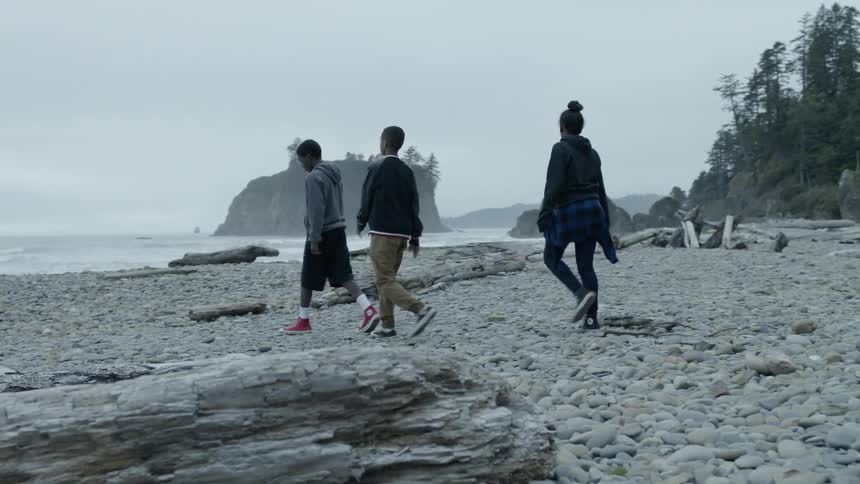 Three teenagers on a rocky shore walk towards the water