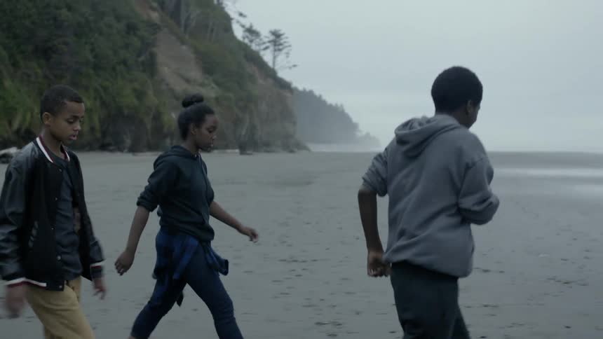 Three black teenagers walk across pacific northwest beach under overcast sky