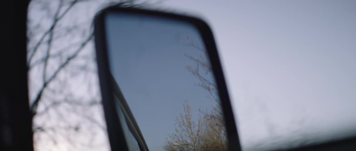 Reflection of trees and sky in car side mirror in motion