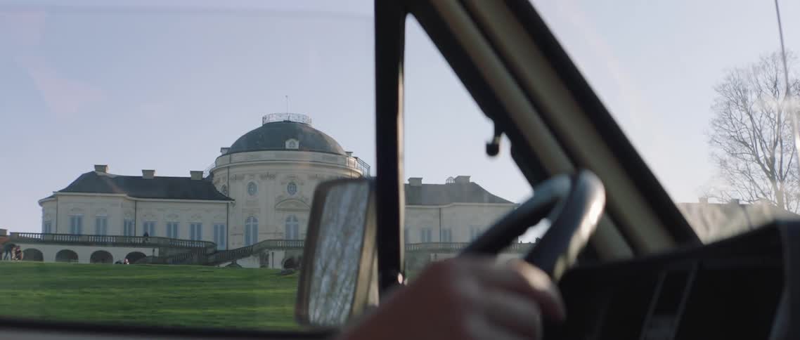 Driver drives a vehicle past a large building and crowd of people
