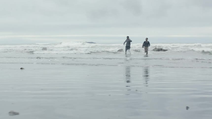 A pair of boys playing and running along a beach on a cloudy day